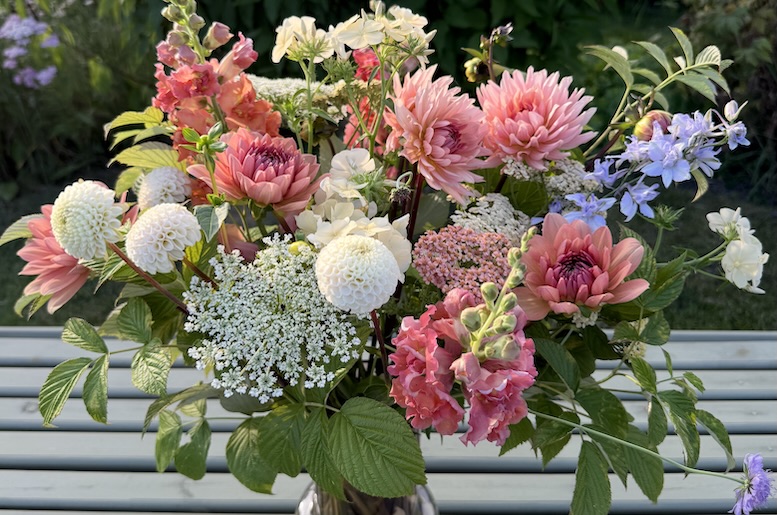 Färgstark bukett med rosa, vita och blå blommor i en kruka mot grön bakgrund.